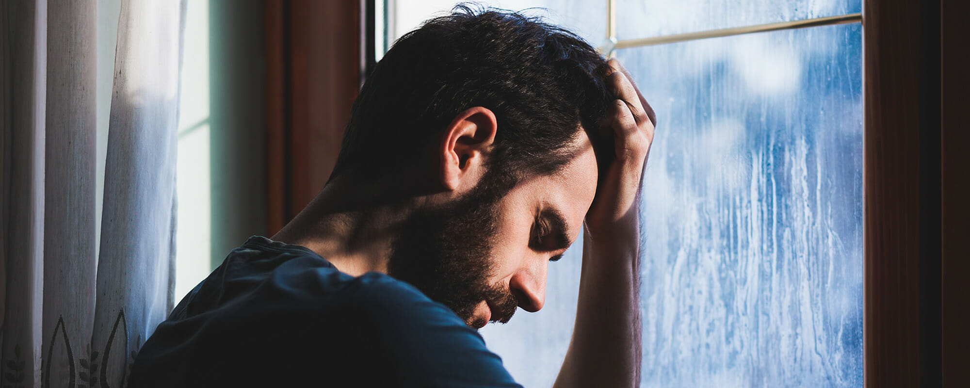 Man standing by window with his head in his hands