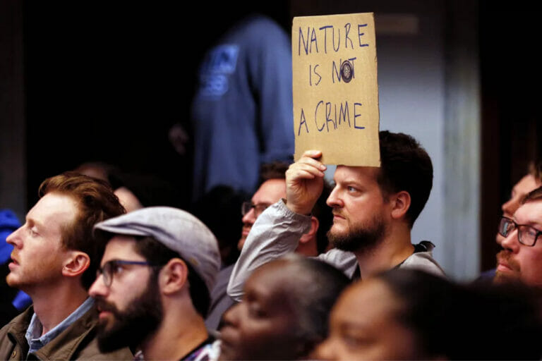 Crowd of people listening to a speaker. One person is holding a sign that says Nature is not a crime.
